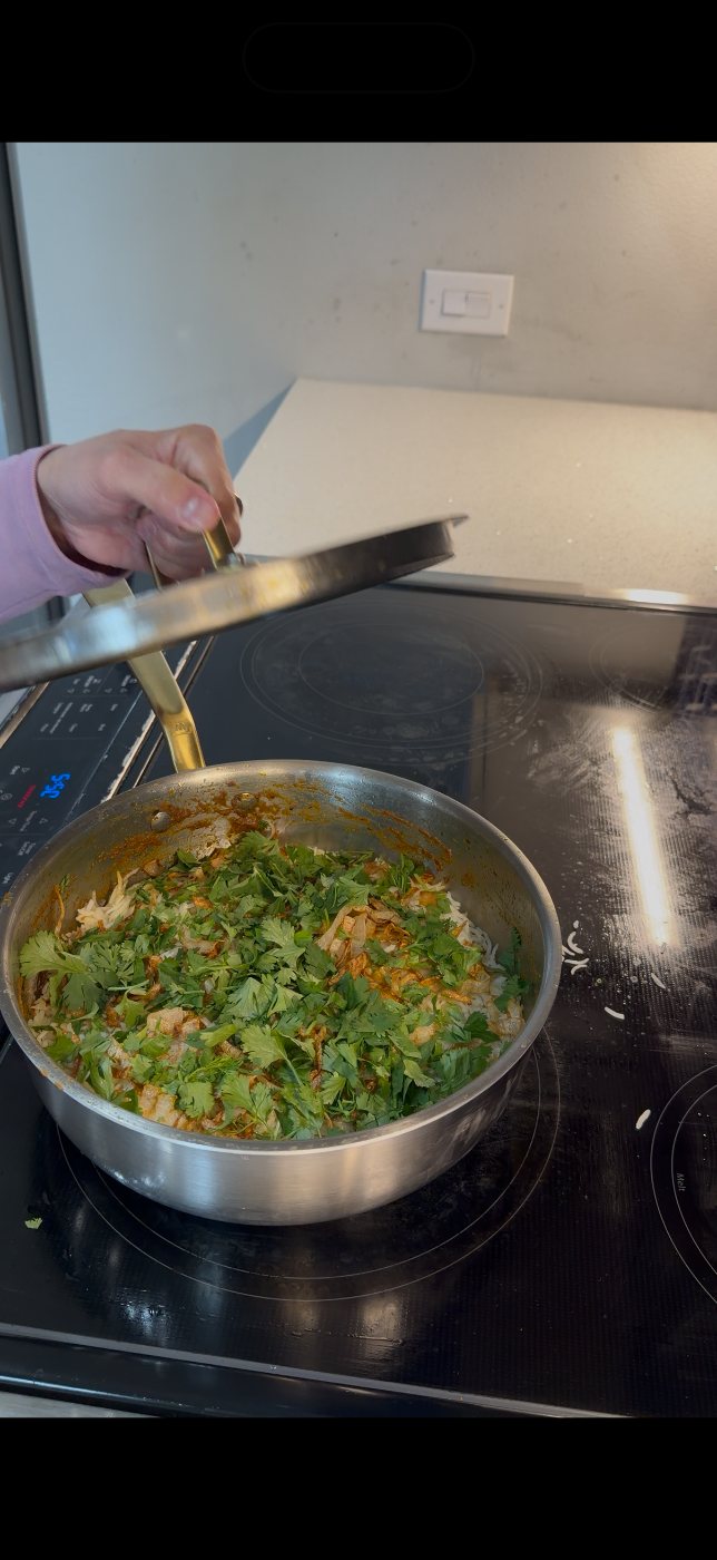 Chicken biryani finished with coriander and fried onions in a stainless saucier