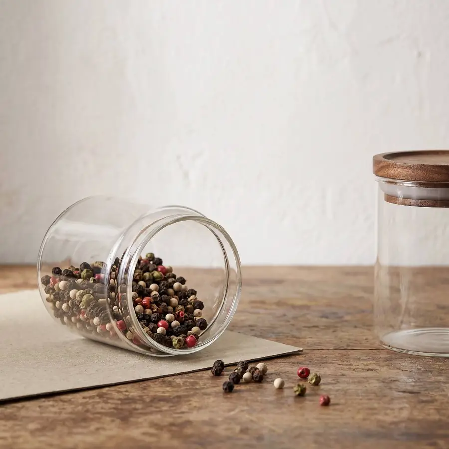 A tipped glass jar spilling peppercorns onto a wooden board